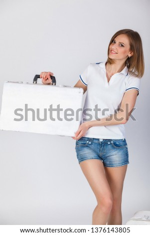Beautiful girl in a t-shirt and denim shorts fun posing with a suitcase on a white background. Fun photo. White background.