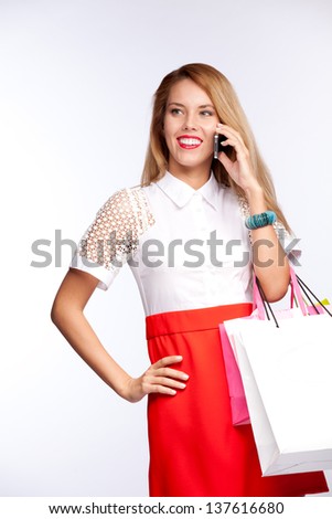 Happy beautiful woman with shopping  gift bags talking on cellular mobile phone, cheerful smiling on a white background
