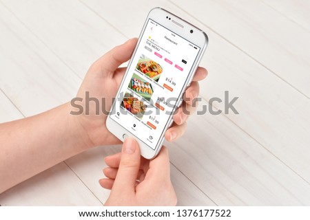 Girl while sitting at the table ordering food on her smartphone with food delivery app