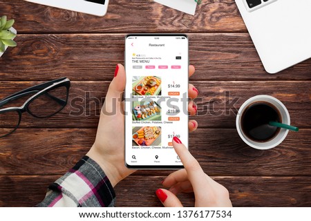 Girl sitting at the office desk and ordering food on her smartphone with food delivery app