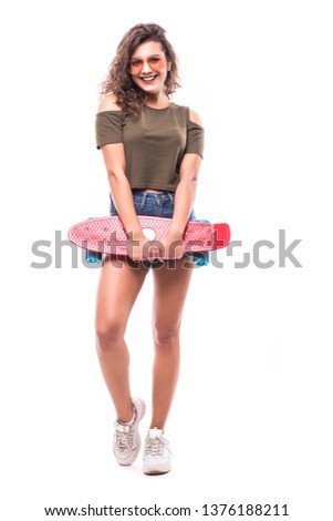 Full length portrait of a pretty young woman in sunglasses posing with skateboard while standing and looking at camera over white background