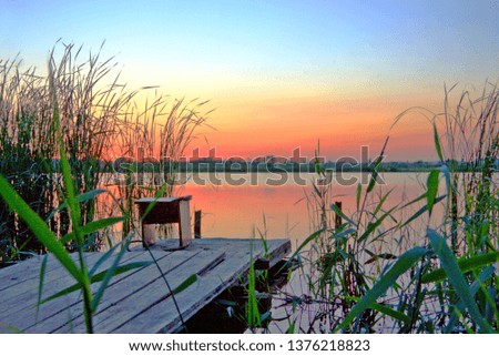 Beautiful blue sky on the lake. A ragged picture. Sunset or dawn. A wooden bridge with a bench. Place for fishing.