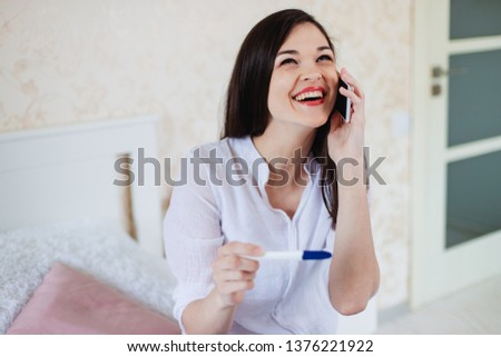 Young woman rejoices while looking at a positive pregnancy test. reports the slavery news to her husband by phone