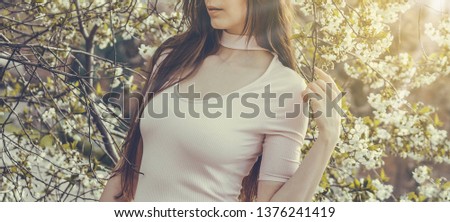 Beautiful girl with spring cherry flowers, sunshine backlit. Pretty young brunette woman's hand touching a blooming tree branches. Fashion, happiness and lifestyle concept. 