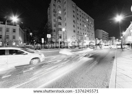 Night city on a long exposure, black and white.
Street of the night city with passing cars and traces of lights. 