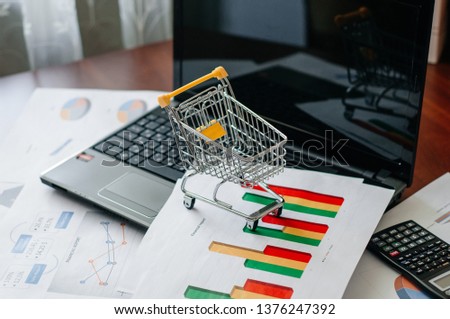 Selective focus of toy shopping bag in small shopping trolley with laptop on background