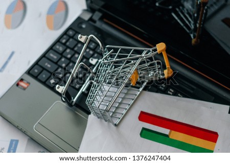 Selective focus of toy shopping bag in small shopping trolley with laptop on background