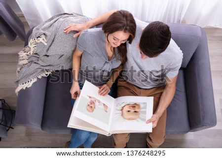 High Angle View Of An Couple Sitting On Sofa Looking At Photo Album