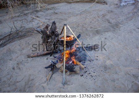 mulled wine with fruit in a large metal cauldron cooked on a fire on gray sand with dry firewood