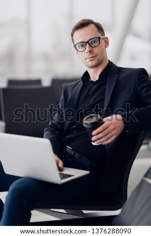 Handsome businessman writing massages with cup of coffee in airport