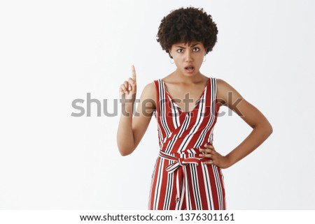 No I forbid you. Strict and bossy attractive female dark-skinned employer in striped overalls waving index finger in stop or refusal gesture holding hand on hip being displeased and serious Royalty-Free Stock Photo #1376301161
