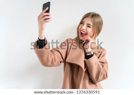 Pretty hipster girl with red lips and beautiful smile taking selfie on white background