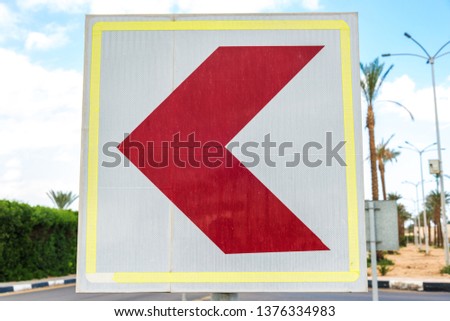 Square white road sign with a red arrow turned to the left