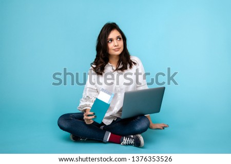 Young woman sitting on the floor with laptop and passport buying tichets online.