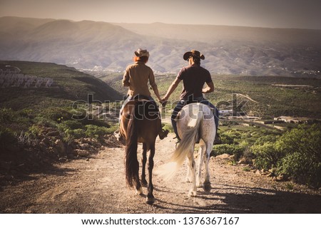 Romantic couple wide horses together holding hands with love and romance in outdoor leisure lifestyle alternative activity - viewed from back young people with aninmals