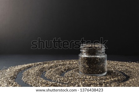 Small jar with chia seeds on black background. Copy space. Chia superfood ingredient concept.