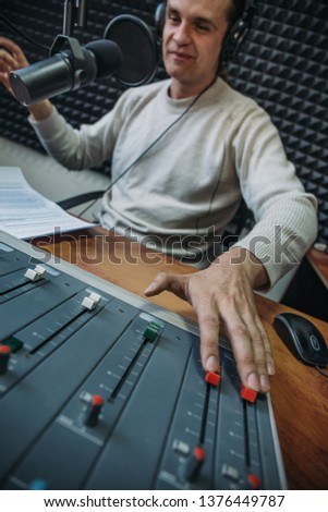 Happy smiling male radio presenter or host with headphones on head talking into microphone in radio station, portrait at workplace, toned