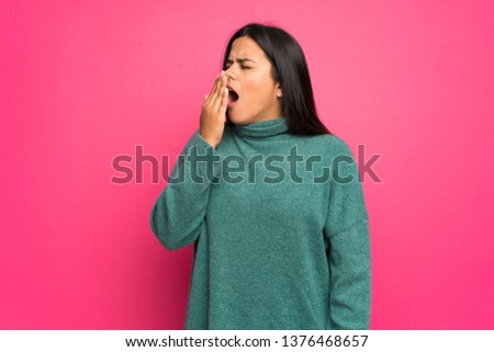 Young Colombian girl with green sweater yawning and covering wide open mouth with hand