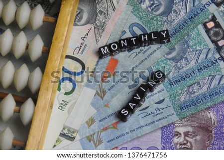 Business concept of Monthly Saving word from plastics cube with bank notes on the background.