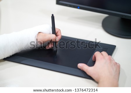 Artist with broken arm drawing something with graphic tablet. Hold pen in broken fractured arm in plaster cast