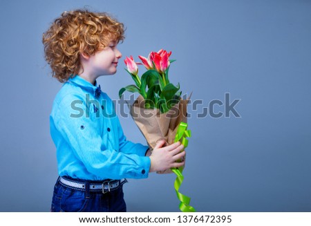 Cute adorable boy holding tulips flowers. Mothers Day. Spring day. Portrait of a happy little boy. Kid holds tulips as gift for mom. International Women's Day. 
