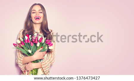 Beauty girl holding Spring tulips Flower bouquet and smiling. Happy Beautiful woman receiving a Bunch of colorful Tulip flowers. Surprised model. Valentine's Day gift. Mother's Day. Birthday party 