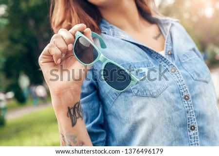 Young woman walking outdoors in the city park holding sunglasses close-up
