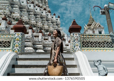 Elegant Asian traveler holding brown basket standing on the stairs at temple in Bangkok, Thailand at afternoon.
