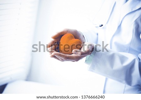 Close-up of unknown female doctor with stethoscope holding heart near the window in hospital.