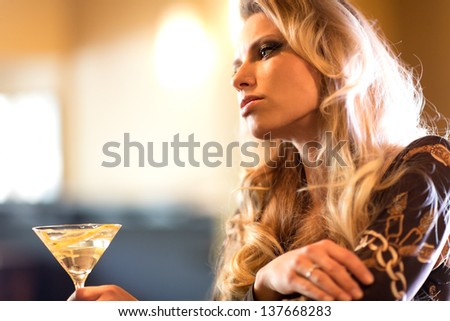 Attractive young woman with a glass cocktail in hand absorbed in thoughts