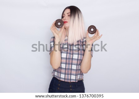 Portrait of cheerful young blonde woman wearing casual wear standing isolated over white background , posing, holding donuts