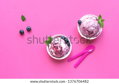 Blueberry Ice Cream on pink background, top view, copy space. Scoop of gelato in cups with blueberries and mint.