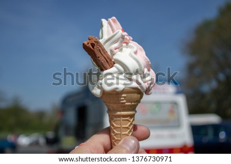 Ice creams cone with a chocolate flake taken on a beautiful blue sky day. with the ice cream truck in the background.
