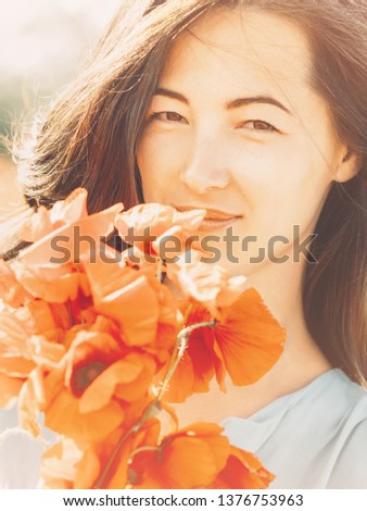 Close-up portrait of smiling beautiful brunette young woman with bouquet of poppies flowers, looking at camera.