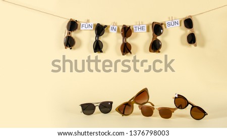 Sunglasses sale concept. Different sunglasses hanging on the rope with phrase hello summer on yellow background. Fashion summer accessories. Copy space