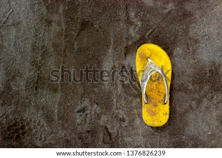 Only one dirty yellow sandal on the black sand. Horor concept.