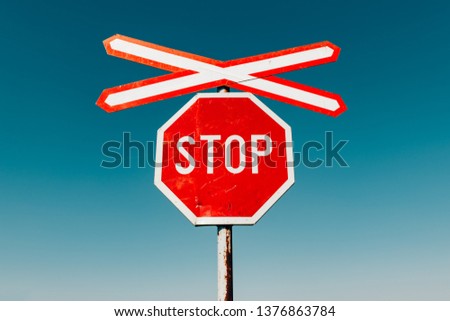 Crossbuck and stop sign on countryside road and railway intersection against blue sky