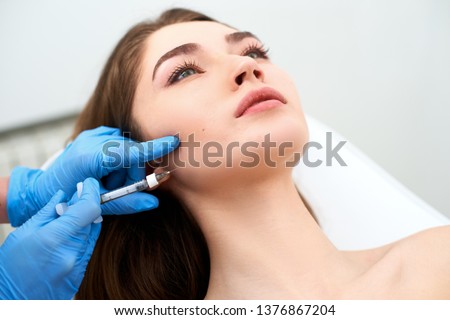 Beautician doctor with filler syringe making injection to jowls. Masseter lines reduction and face contouring therapy. Anti-aging treatment and face lift in cosmetology clinic. Patient lying on chair Royalty-Free Stock Photo #1376867204