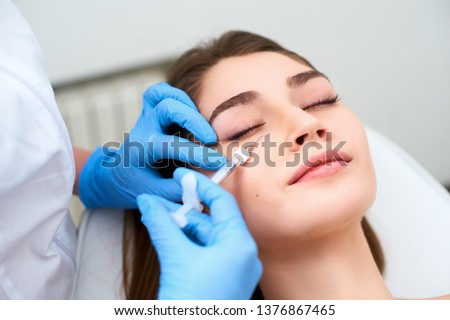 Doctor in medical gloves with syringe injects botulinum under eyes for rejuvenating wrinkle treatment. Filler injection for eye wrinkles smoothing. Plastic aesthetic facial surgery in beauty clinic Royalty-Free Stock Photo #1376867465