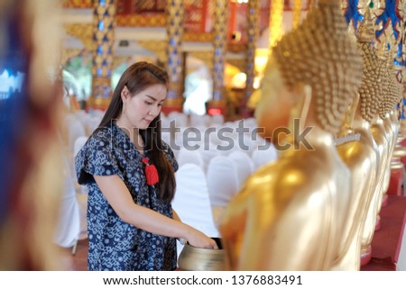 A photograph of an Asian woman dressed in a blue traditional cloth is making merit within the temple.