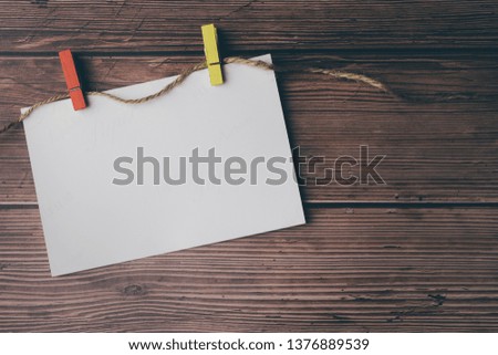 Blank white horizontal poster paper attached with red and yellow clips hung on the wooden wall.