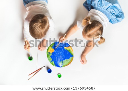 Ecology concept with two prety little kids painting earth on white background, copy space, top view
