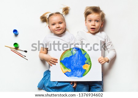 Ecology concept with two prety little kids painting sad earth on white background, copy space, top view