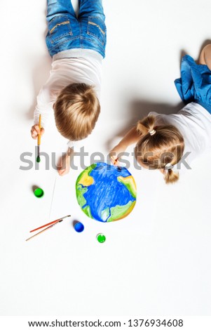 Ecology concept with two prety little kids painting earth on white background, copy space, top view, vertical