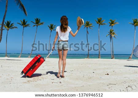 A woman with a red suitcase walks on the beach palm rest relaxation