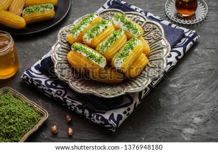 Arabic Cuisine: Middle Eastern dessert/Ramadan dessert "Balah Al-Sham "or "Balah El Shaam" with cream filling and crushed pistachio.Served with honey syrup and oriental tea. Close up with copy space. Royalty-Free Stock Photo #1376948180