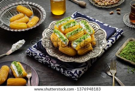Arabic Cuisine: Middle Eastern dessert/Ramadan dessert "Balah Al-Sham "or "Balah El Shaam" with cream filling and crushed pistachio.Served with honey syrup and oriental tea. Close up with copy space. Royalty-Free Stock Photo #1376948183