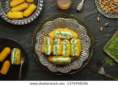Arabic Cuisine: Middle Eastern dessert/Ramadan dessert "Balah Al-Sham "or "Balah El Shaam" with cream filling and crushed pistachio.Served with honey syrup and oriental tea.Top view with close up. Royalty-Free Stock Photo #1376948186