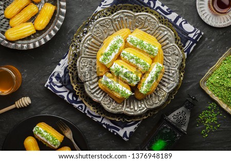 Arabic Cuisine: Middle Eastern dessert/Ramadan dessert "Balah Al-Sham "or "Balah El Shaam" with cream filling and crushed pistachio.Served with honey syrup and oriental tea.Top view with close up. Royalty-Free Stock Photo #1376948189