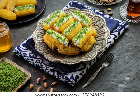 Arabic Cuisine: Middle Eastern dessert/Ramadan dessert "Balah Al-Sham "or "Balah El Shaam" with cream filling and crushed pistachio.Served with honey syrup and oriental tea. Close up with copy space. Royalty-Free Stock Photo #1376948192